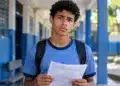 Estudante de uniforme azul segura um documento escolar com expressão de dúvida, representando quem pode ficar sem os R$ 200 do Incentivo-Enem do Pé-de-Meia.