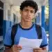 Estudante de uniforme azul segura um documento escolar com expressão de dúvida, representando quem pode ficar sem os R$ 200 do Incentivo-Enem do Pé-de-Meia.