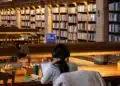 Estudante lê e estuda com livros em mesa de biblioteca escolar
