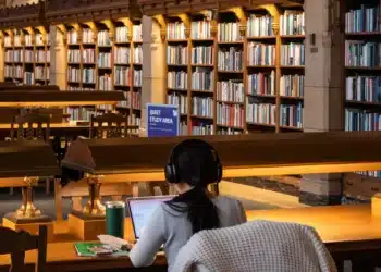 Estudante lê e estuda com livros em mesa de biblioteca escolar