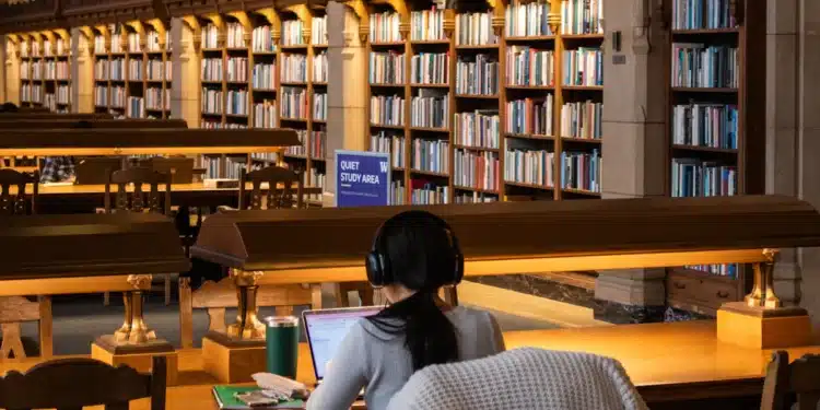 Estudante lê e estuda com livros em mesa de biblioteca escolar