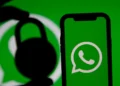 Logotipo do WhatsApp na tela de um celular, com a silhueta de um cadeado à esquerda e fundo verde.