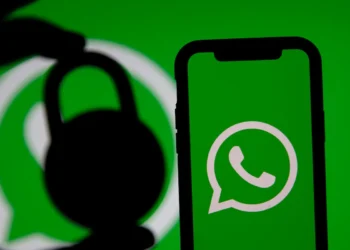 Logotipo do WhatsApp na tela de um celular, com a silhueta de um cadeado à esquerda e fundo verde.