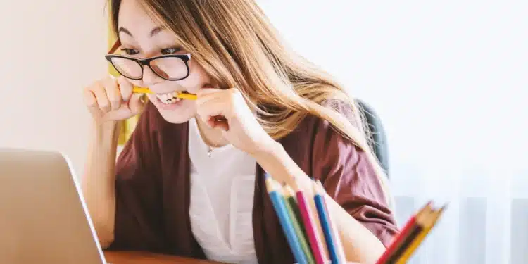Mulher estuda em frente ao computador com lápis na mão, cena que ilustra o curso de Português online de 80 horas