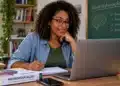 Professora mexendo no notebook, com livro de neuroeducação sobre a mesa, representando o curso online de Formação de Professores em Neuroeducação oferecido pelo MEC.