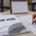 Mão preenche cartão de respostas ao lado de prova impressa ENEM 2026 e calendário em mesa, simbolizando as datas do Enem 2026.