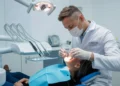 Cirurgião-dentista com máscara e luvas realiza atendimento em paciente na cadeira odontológica.