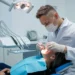 Cirurgião-dentista com máscara e luvas realiza atendimento em paciente na cadeira odontológica.