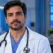 Médico de jaleco branco e estetoscópio em ambiente hospitalar, com vitral religioso ao fundo, representando a origem cristã do Dia do Médico.