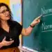 Professora aponta para as palavras normalizar e normatizar escritas no quadro-negro durante explicação em sala de aula.
