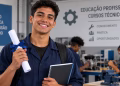 Imagem ilustrativa de jovem sorridente de uniforme azul segurando um diploma enrolado e um caderno em uma oficina de ensino técnico, com outros alunos ao fundo, em referência às regras do diploma de curso técnico