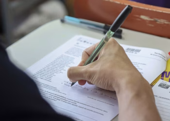 Imagem ilustrativa de candidato escrevendo no caderno de prova com caneta transparente, em referência ao local de prova da Fuvest 2027