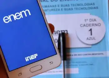 Celular com identificação do Enem em frente a caderno de prova do exame.