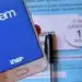 Celular com identificação do Enem em frente a caderno de prova do exame.