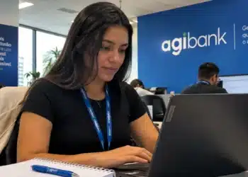 Jovem profissional utilizando notebook em escritório com identidade visual do Agibank, representando as oportunidades de estágio com bolsa-auxílio de R$ 2.400.