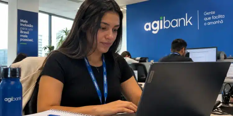 Jovem profissional utilizando notebook em escritório com identidade visual do Agibank, representando as oportunidades de estágio com bolsa-auxílio de R$ 2.400.