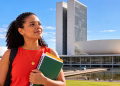 Imagem ilustrativa de jovem universitária com mochila e cadernos diante do Congresso Nacional, em Brasília, em referência ao estágio na Câmara dos Deputados