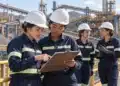 Quatro mulheres com equipamentos de proteção discutem uma análise técnica em uma instalação de mineração ao ar livre, simbolizando o Programa de Estágio 2027 da Samarco, exclusivo para mulheres.