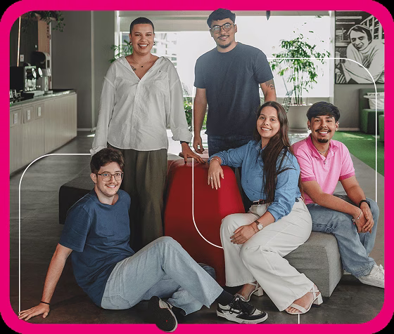 Cinco jovens reunidos em uma área de convivência de escritório, sentados e em pé ao redor de um banco vermelho, em imagem de divulgação do estágio Serasa Experian