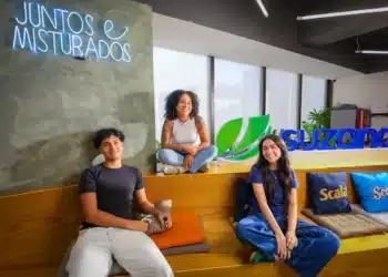Três jovens em ambiente da Suzano, ao lado do logotipo da empresa e de um letreiro com a frase “Juntos e misturados”.