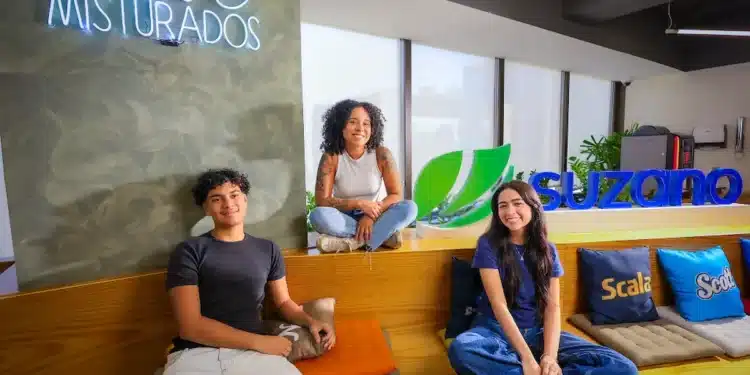 Três jovens em ambiente da Suzano, ao lado do logotipo da empresa e de um letreiro com a frase “Juntos e misturados”.