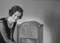 Mulher ajusta rádio antigo sobre a mesa, lembrança de quando estudar a distância era pelo rádio e pelo correio