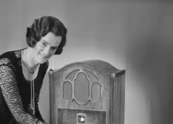 Mulher ajusta rádio antigo sobre a mesa, lembrança de quando estudar a distância era pelo rádio e pelo correio