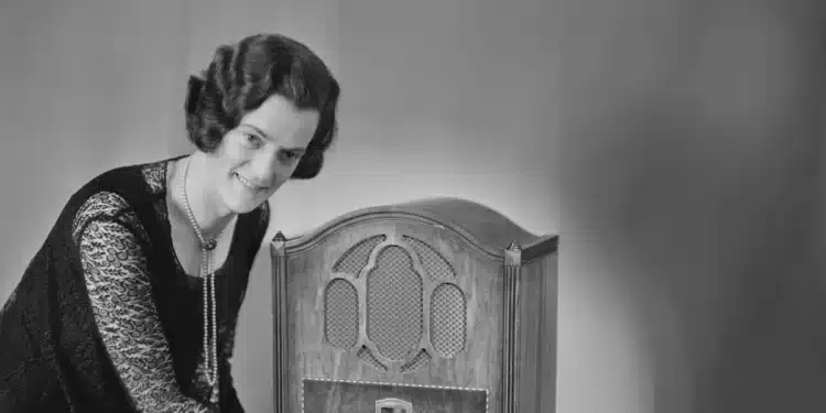Mulher ajusta rádio antigo sobre a mesa, lembrança de quando estudar a distância era pelo rádio e pelo correio