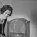Mulher ajusta rádio antigo sobre a mesa, lembrança de quando estudar a distância era pelo rádio e pelo correio
