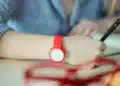 Estudante com relógio vermelho no pulso escreve durante prova, ilustrando os horários do Enem 2026