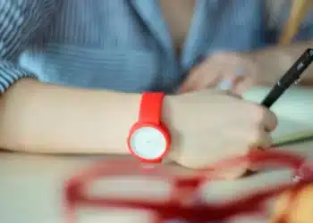 Estudante com relógio vermelho no pulso escreve durante prova, ilustrando os horários do Enem 2026