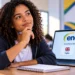 Jovem negra de cabelos cacheados pensa segurando caneta diante de notebook com tela do ENEM mostrando opções de prova em inglês e espanhol.