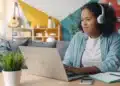 Jovem de fones de ouvido estuda no notebook em casa, rotina de quem faz curso de inglês básico online