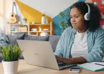 Jovem de fones de ouvido estuda no notebook em casa, rotina de quem faz curso de inglês básico online