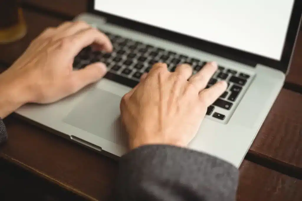 Pessoa utilizando notebook, com as mãos posicionadas sobre o teclado, representando a inscrição online para o Exame de Suficiência.