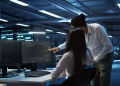 Imagem ilustrativa de dois profissionais de tecnologia analisando códigos em monitores dentro de um centro de dados, área de atuação ligada às bolsas do curso da Cisco