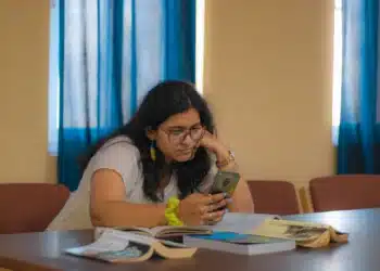 Mulher sentada à mesa olhando o celular, como quem faz a justificativa do 2º turno pelo aplicativo