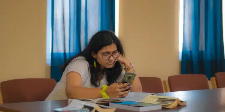 Mulher sentada à mesa olhando o celular, como quem faz a justificativa do 2º turno pelo aplicativo