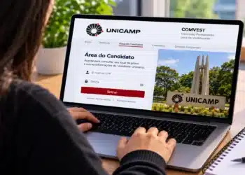 Jovem acessa área do candidato Unicamp pelo notebook com login e imagem do campus, simbolizando a consulta aos locais de prova do vestibular da Unicamp.