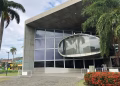 Fachada de uma das Naves do Conhecimento no Rio de Janeiro, prédio de concreto com grande janela oval espelhada e palmeiras na entrada