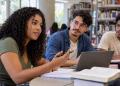 Três estudantes reunidos em uma biblioteca, com notebook, livros e cadernos sobre a mesa, simbolizando as diferenças entre as modalidades e a proposta universitária.