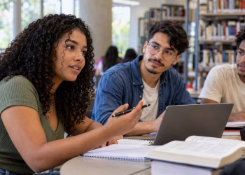 Três estudantes reunidos em uma biblioteca, com notebook, livros e cadernos sobre a mesa, simbolizando as diferenças entre as modalidades e a proposta universitária.