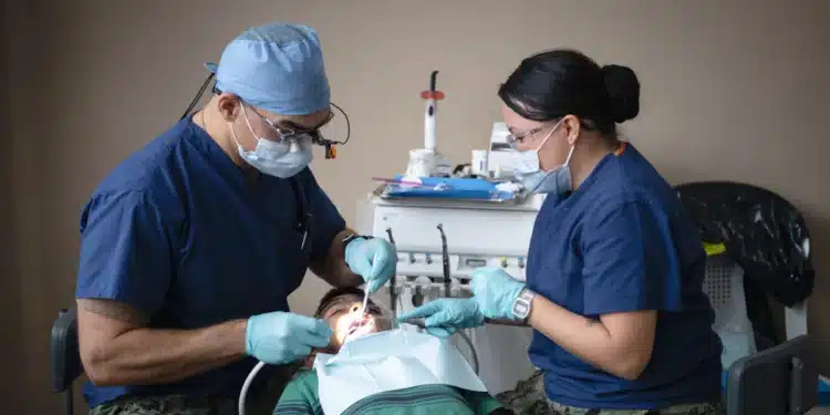 Dentista e profissional técnico em saúde bucal atendem paciente juntos em consultório odontológico