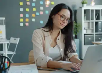 Jovem usa notebook em escritório, cena ligada a curso de informática com sistema, arquivos, internet e Excel