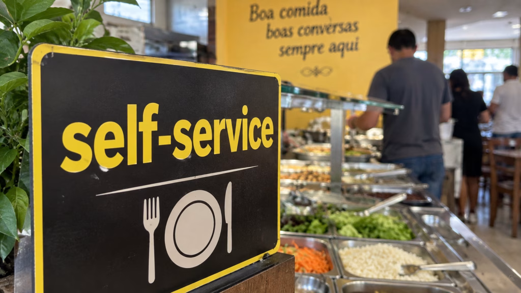 Imagem ilustrativa de placa preta com a palavra self-service em amarelo e o desenho de prato e talheres, à frente de um bufê em que clientes se servem