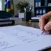 Mão segurando uma caneta azul e assinando um documento com várias assinaturas, representando um abaixo-assinado.