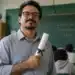 Professor com diploma de pós-graduação nas mãos, em sala de aula, representando a valorização salarial pela qualificação profissional.