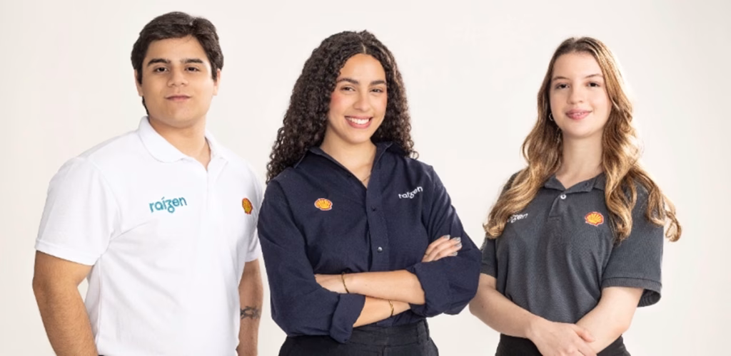Três jovens com camisas da Raízen e da Shell posam lado a lado em fundo branco