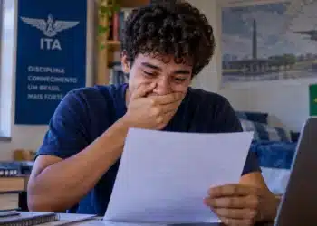 Jovem candidato confere resultado em papel, representando a divulgação dos aprovados na primeira etapa do Vestibular ITA 2027.