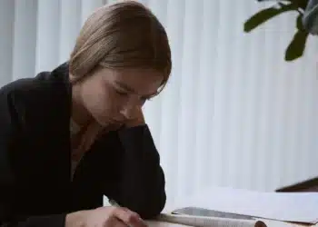 Jovem estudando com livro aberto na mesa durante a revisão para o Enem nos 15 dias antes da prova